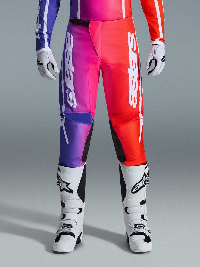 Alpinestars 2026 Fluid Apex Pants, pantaloni da motocross, design sfumato multicolore viola, rosa e rosso, grande logo Alpinestars bianco sulle gambe, abbinati a stivali e guanti da motocross bianchi e neri, abbigliamento professionale per fuoristrada