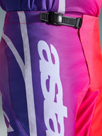 Alpinestars 2026 Fluid Apex Pants, pantaloni da motocross, multicolore viola, rosa e rosso, primo piano della zona vita e fianchi con sistema di chiusura a cricchetto nero e grande logo Alpinestars verticale bianco, design sfumato vivace con trama in tessuto poliestere resistente