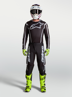 Alpinestars pantaloni Fluid Apex V2, neri e argento, da motocross uomo, con stivali giallo neon, casco e maglia da corsa.