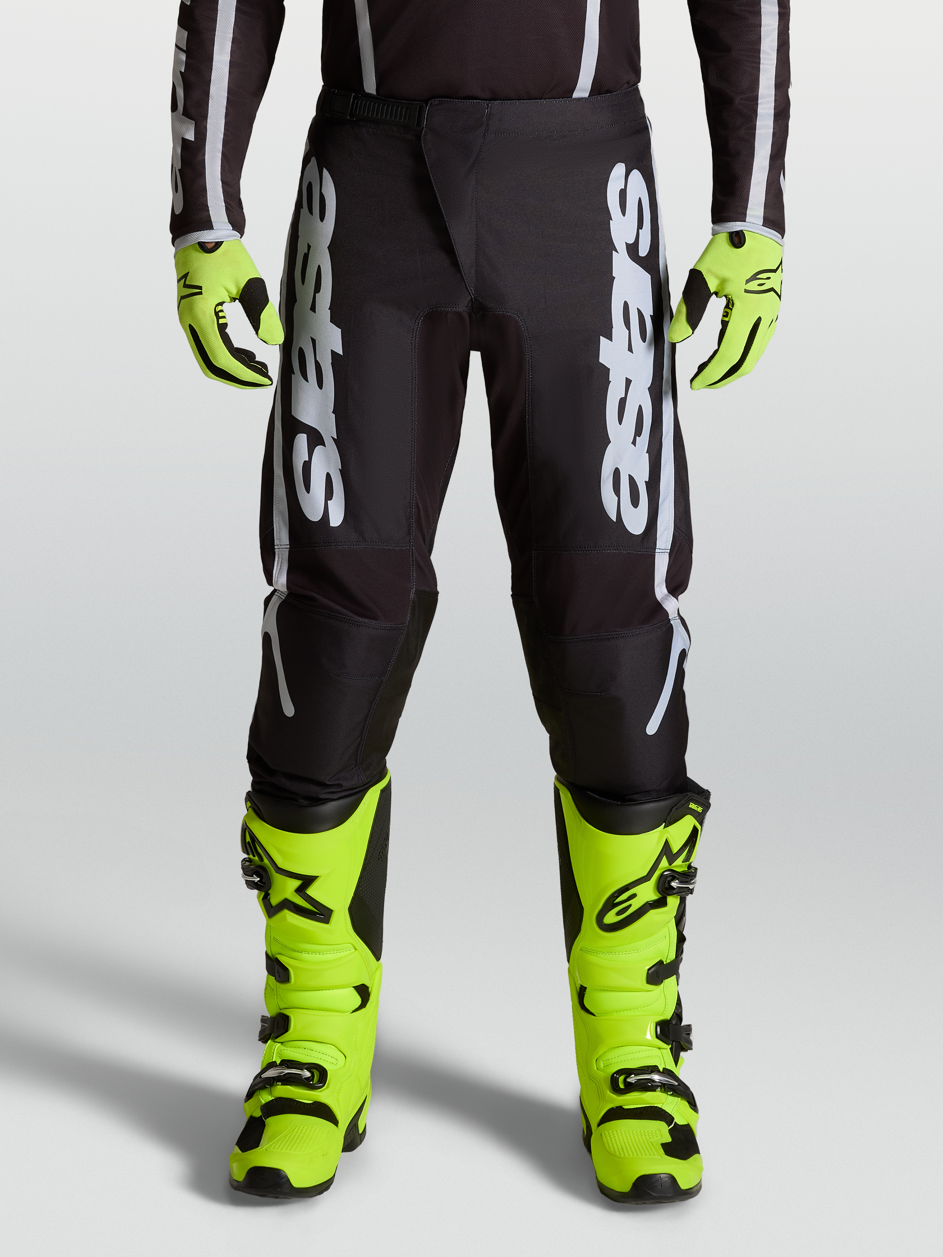 Alpinestars Pantaloni Fluid Apex V2, pantaloni motocross da uomo, nero e argento, indossati con stivali e guanti giallo fluo coordinati.