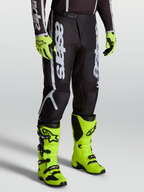 Alpinestars Pantaloni Fluid Apex V2, pantaloni motocross da uomo, nero e argento, indossati con stivali giallo fluo.