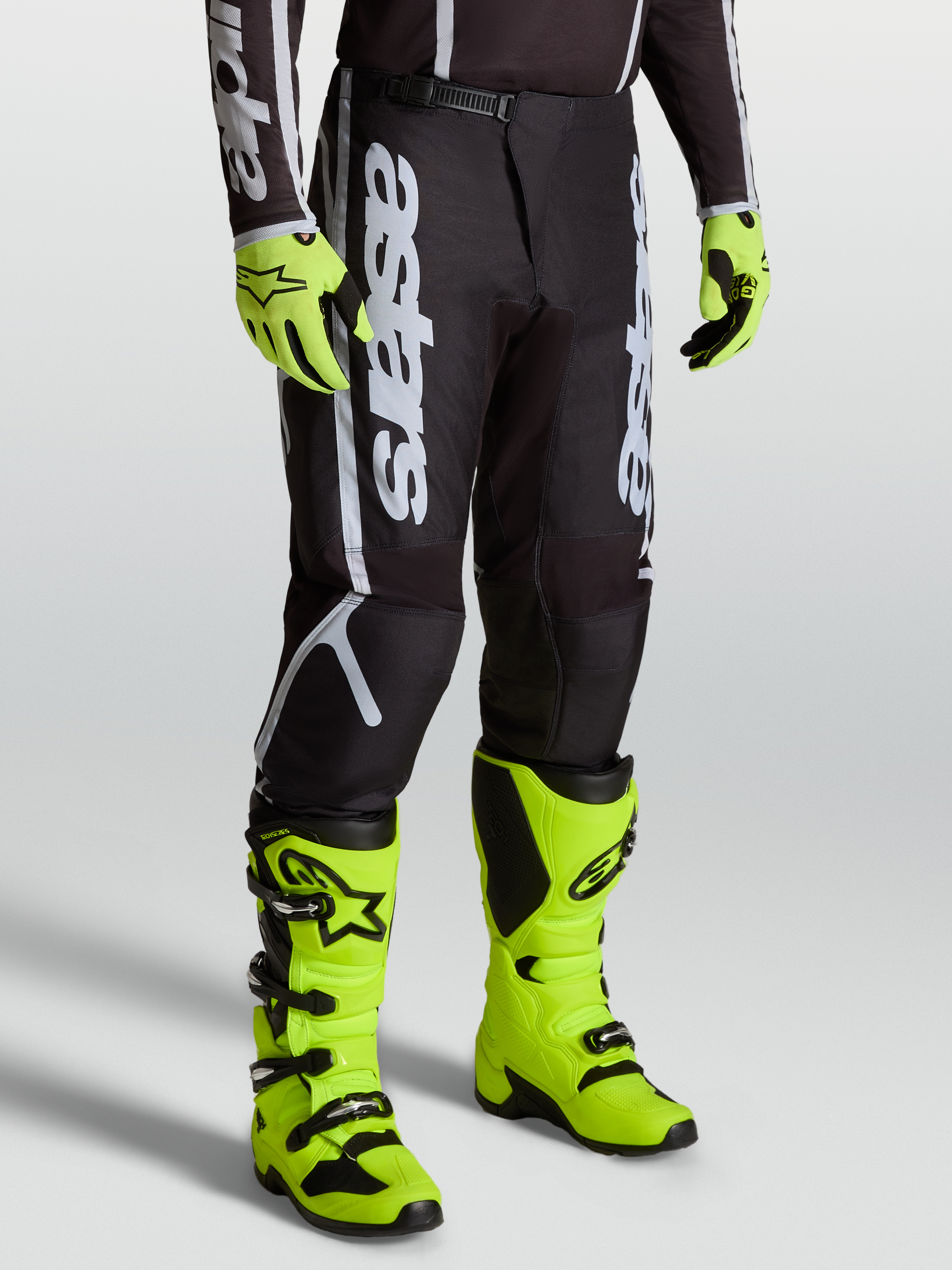 Alpinestars Pantaloni Fluid Apex V2, pantaloni motocross da uomo, nero e argento, indossati con stivali giallo fluo.