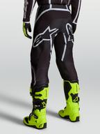 Alpinestars Pantaloni Fluid Apex V2, pantaloni da motocross da uomo, nero e argento con logo bianco, indossati con stivali giallo fluorescente