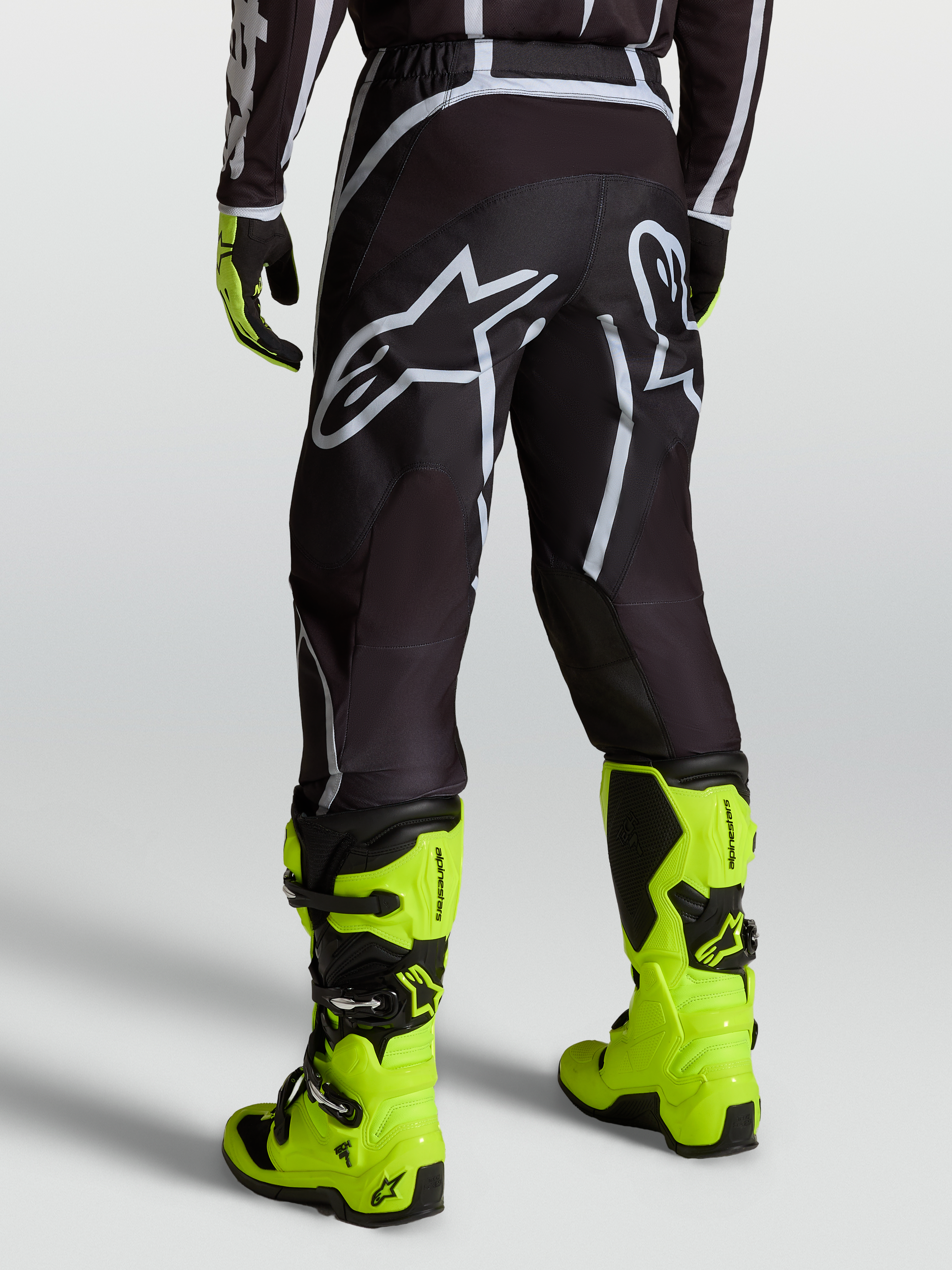 Alpinestars Pantaloni Fluid Apex V2, pantaloni da motocross da uomo, nero e argento con logo bianco, indossati con stivali giallo fluorescente
