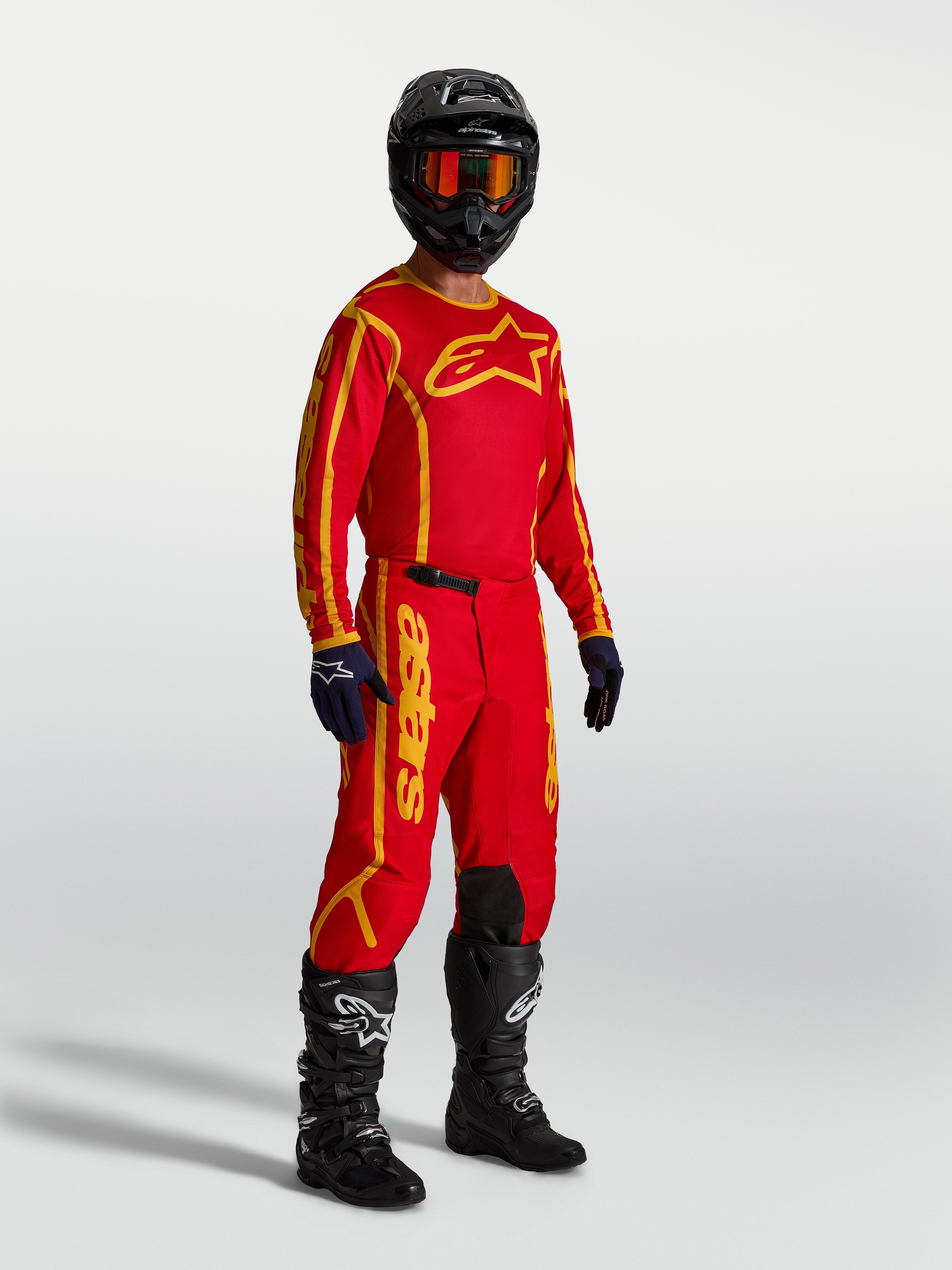 Alpinestars Pantaloni Fluid Apex V2, pantaloni da motocross rossi fuoco e oro da uomo, indossati con maglia e stivali.