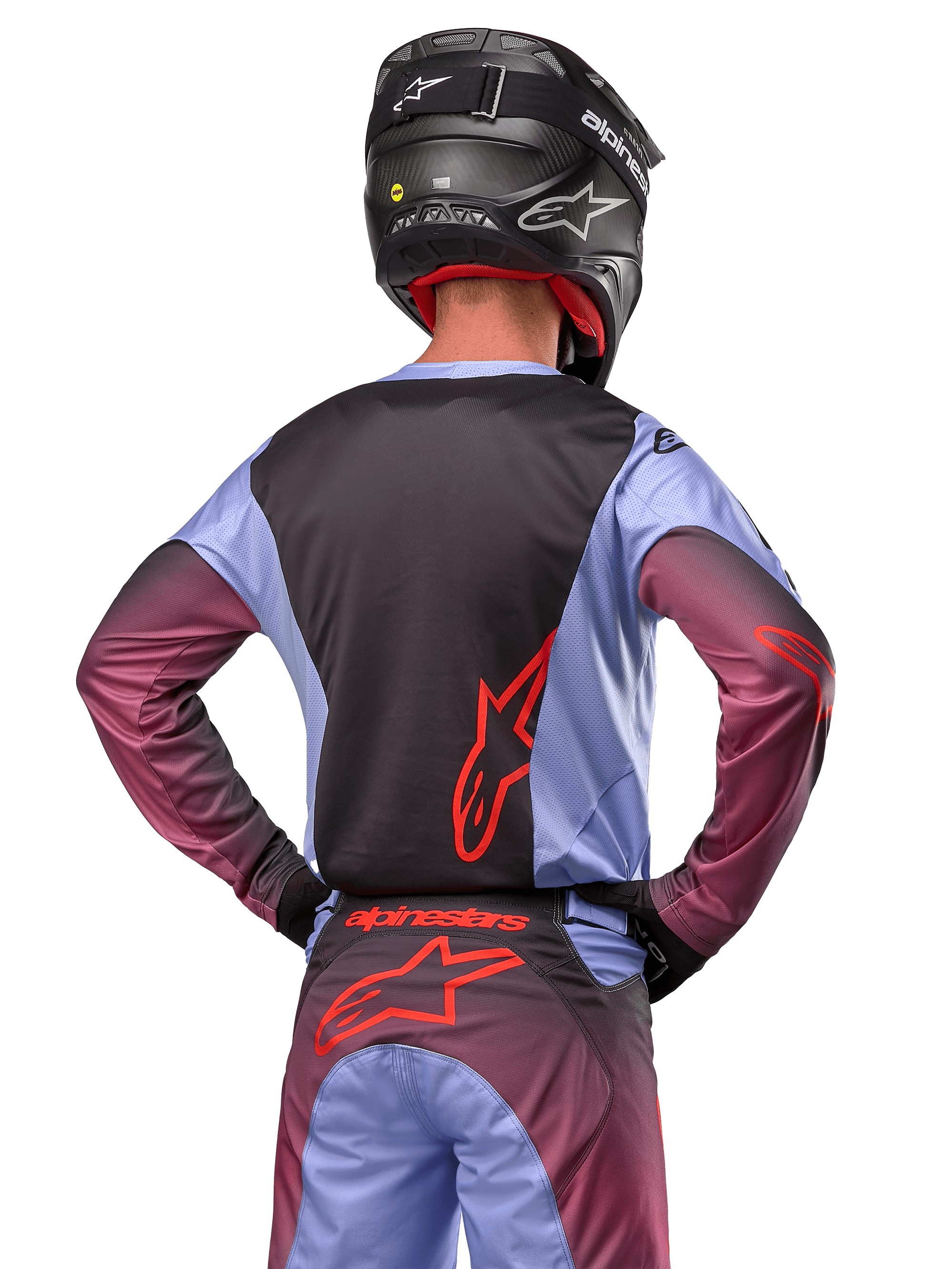 Pilota di motocross visto di spalle con abbigliamento Alpinestars Racer Hoen 2024, maglia Lavan Purple e nera con logo rosso, pantaloni coordinati con dettagli rossi, casco nero, completo coordinato per corse fuoristrada