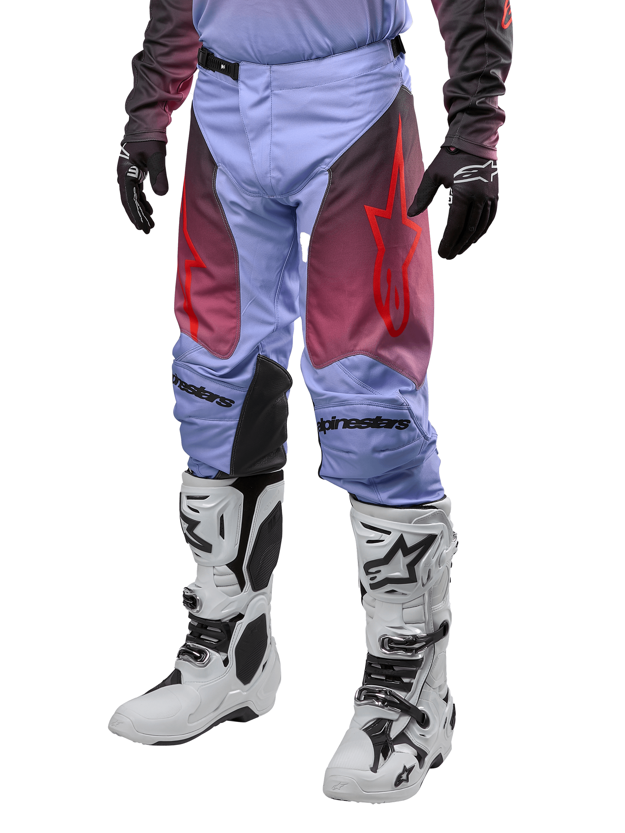 Alpinestars Racer Hoen Pants 2024, pantaloni da motocross, viola Lavan e nero con grafiche rosse, con loghi a stella rossi sulle cosce e scritte nere sulle ginocchia, indossati con stivali bianchi e neri e guanti neri