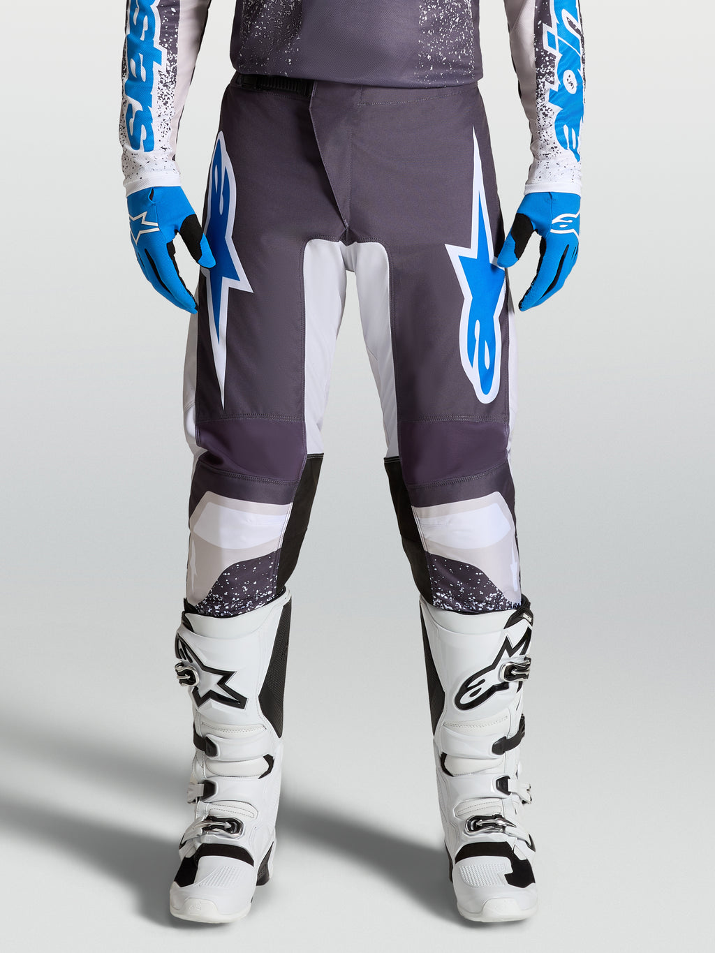 Alpinestars pantaloni Fluid Drag, pantaloni da motocross grigi e blu, design ergonomico con gambe precurvate, indossati da un pilota con stivali bianchi
