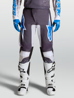 Alpinestars pantaloni Fluid Drag, pantaloni da motocross grigi e blu, design ergonomico con gambe precurvate, indossati da un pilota con stivali bianchi