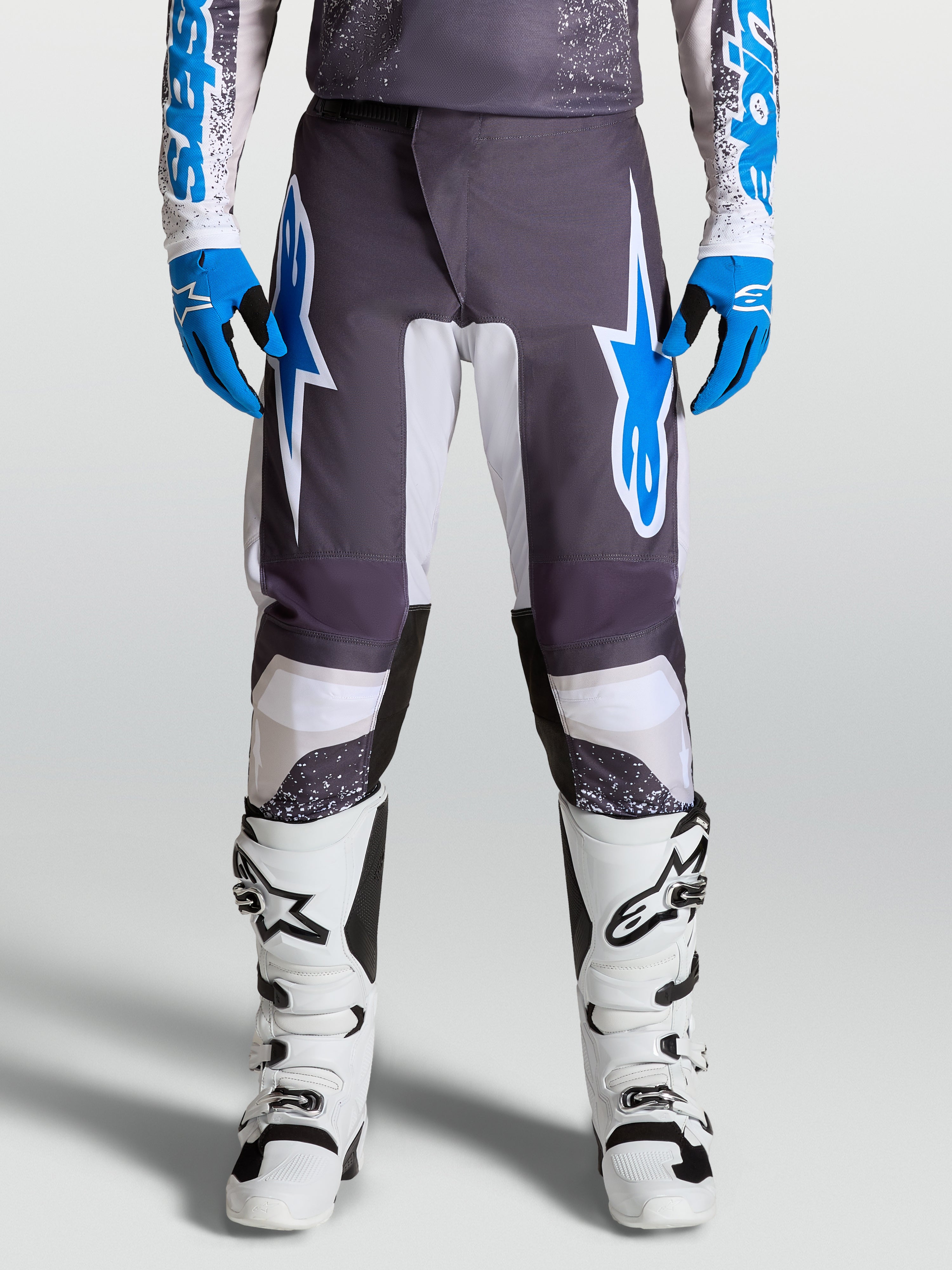 Alpinestars pantaloni Fluid Drag, pantaloni da motocross grigi e blu, design ergonomico con gambe precurvate, indossati da un pilota con stivali bianchi