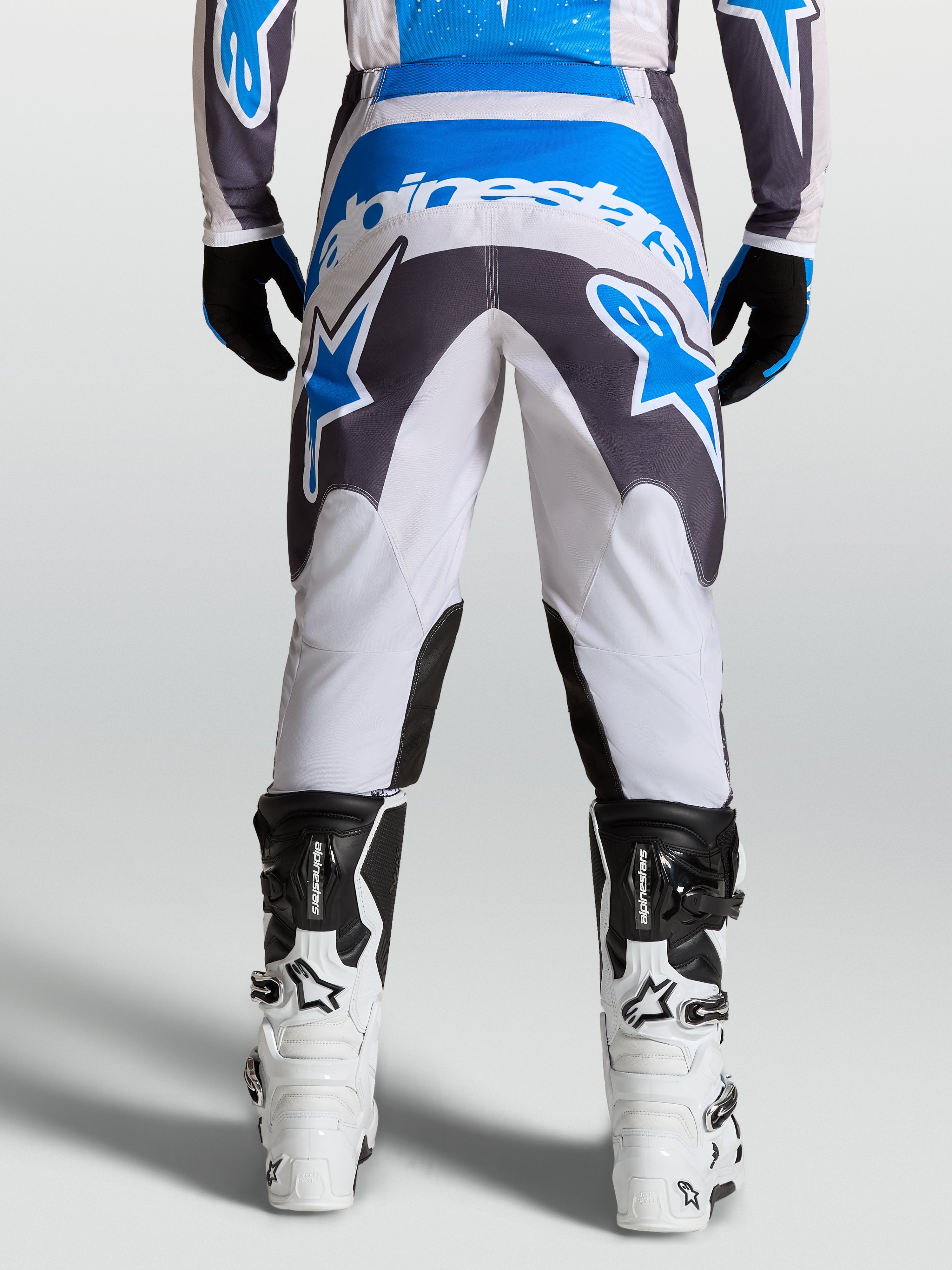 Alpinestars Pantaloni Fluid Drag, pantaloni da motocross per uomo in grigio, blu e bianco, caratterizzati da seduta rinforzata e design ergonomico per la guida off-road, vista posteriore.