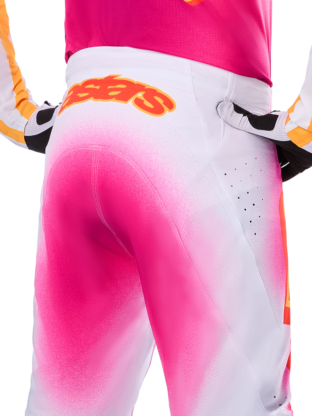 Alpinestars Limited Edition Supertech AFD MIG Pants, pantaloni da motocross, rosa fluo e bianco con un effetto sfumato a spruzzo, grande logo Alpinestars arancione sul girovita posteriore, vista ravvicinata che mostra la vestibilità atletica e le perforazioni per la ventilazione.