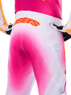 Alpinestars Limited Edition Supertech AFD MIG Pants, pantaloni da motocross, rosa fluo e bianco con un effetto sfumato a spruzzo, grande logo Alpinestars arancione sul girovita posteriore, vista ravvicinata che mostra la vestibilità atletica e le perforazioni per la ventilazione.