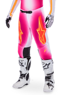 Pantaloni da motocross Alpinestars Supertech AFD MIG Limited Edition, rosa con loghi a stella arancioni e gialli, indossati con stivali da motocross bianchi e guanti bianchi e neri, con pannelli interni alle ginocchia neri e vestibilità atletica, parte di un set da gara ad alte prestazioni
