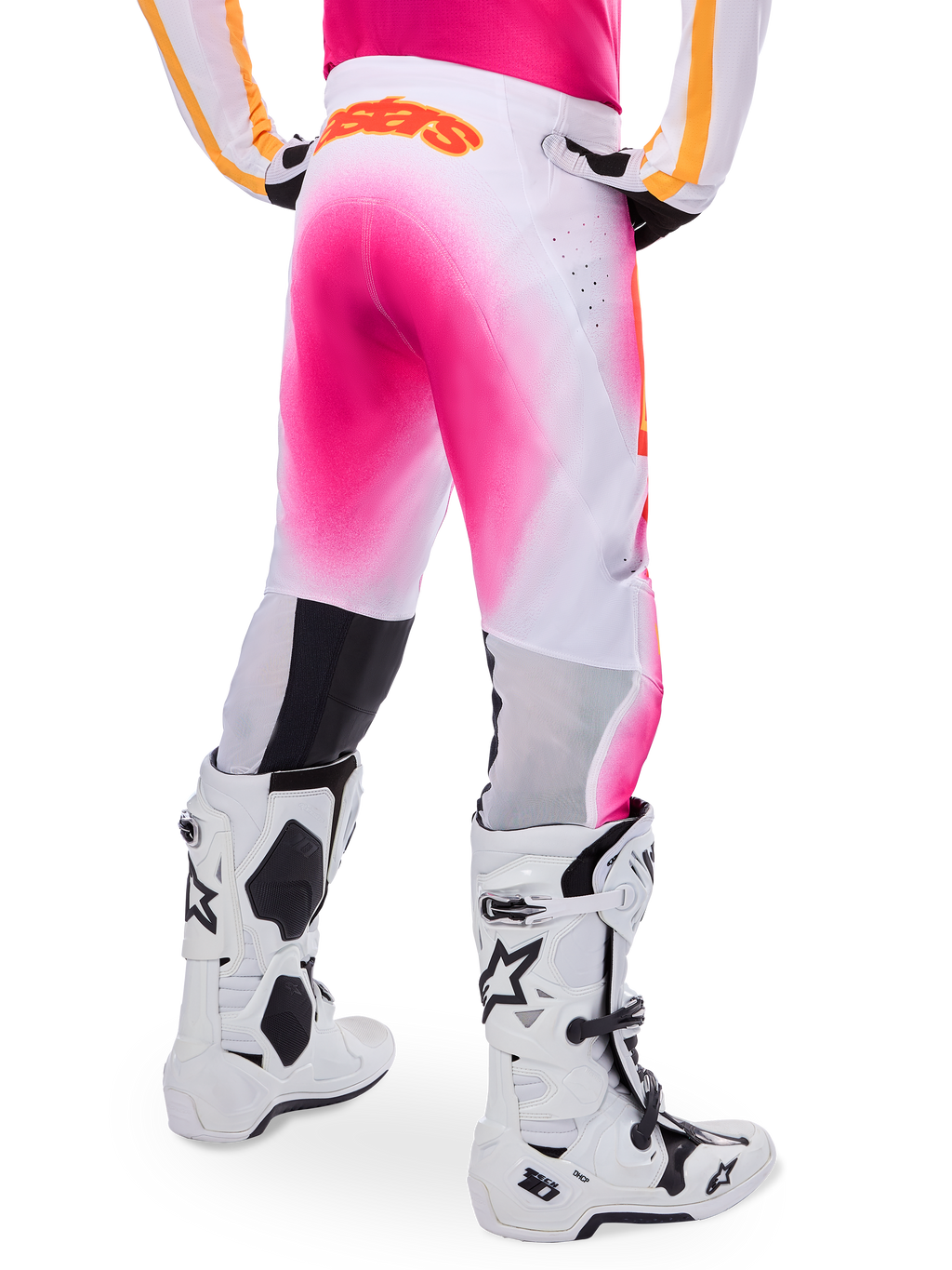 Pantaloni da motocross Alpinestars Supertech AFD MIG Limited Edition, rosa e bianco, vista posteriore con un vivace effetto spray sfumato rosa, logo arancione sulla parte posteriore della vita, abbinati a stivali Tech 10 bianchi e neri, abbigliamento professionale per gare fuoristrada