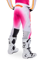 Pantaloni da motocross Alpinestars Supertech AFD MIG Limited Edition, rosa e bianco, vista posteriore con un vivace effetto spray sfumato rosa, logo arancione sulla parte posteriore della vita, abbinati a stivali Tech 10 bianchi e neri, abbigliamento professionale per gare fuoristrada