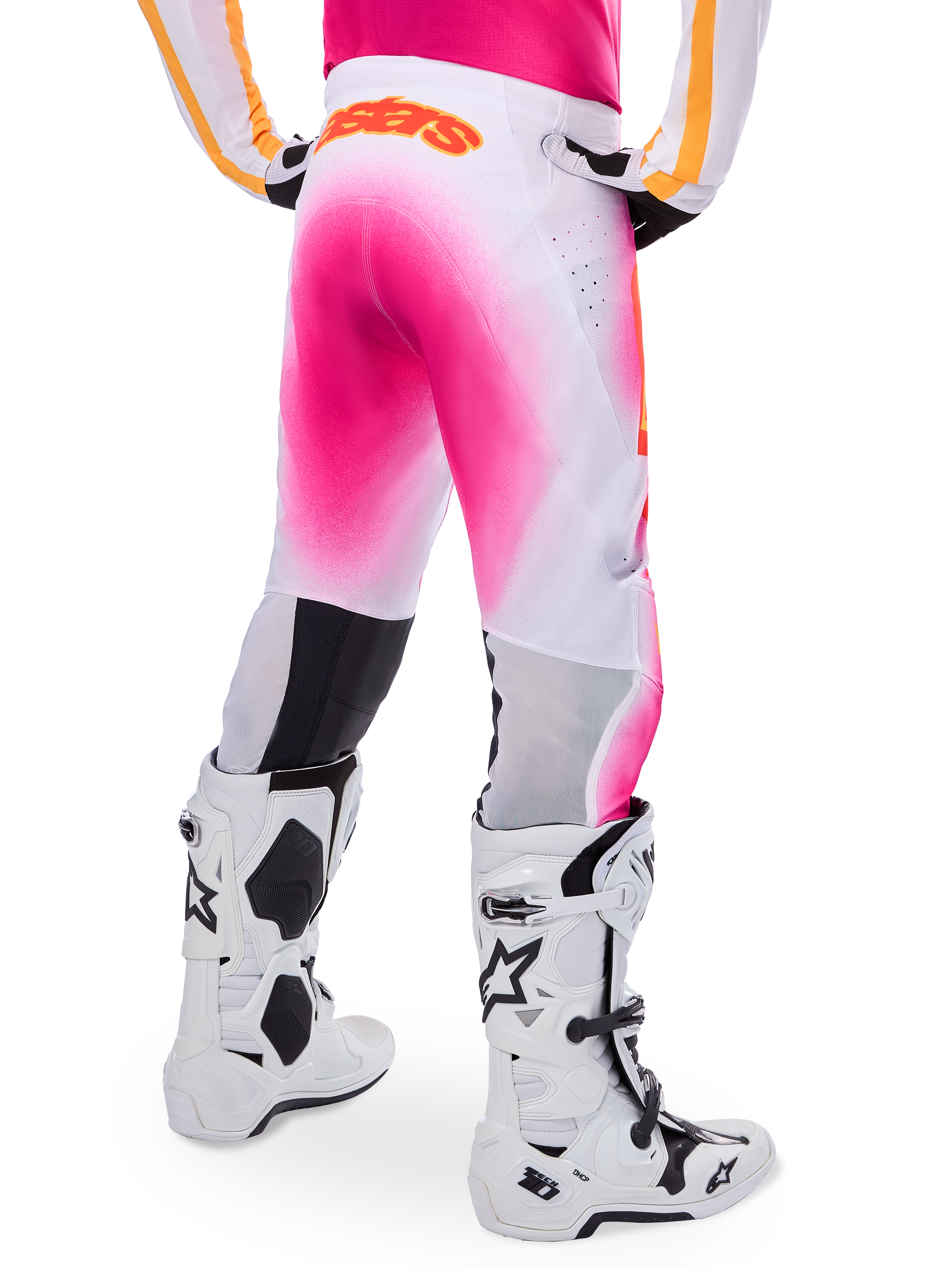 Pantaloni da motocross Alpinestars Supertech AFD MIG Limited Edition, rosa e bianco, vista posteriore con un vivace effetto spray sfumato rosa, logo arancione sulla parte posteriore della vita, abbinati a stivali Tech 10 bianchi e neri, abbigliamento professionale per gare fuoristrada