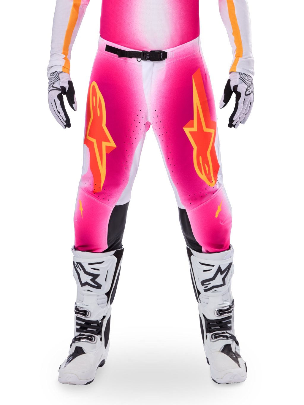 Alpinestars Limited Edition Supertech AFD MIG Pants, pantaloni da motocross, rosa fluo e bianco con accenti arancioni, caratterizzati da grandi loghi a stella sulle cosce, pannelli perforati e zone di grip nere sulle ginocchia, indossati con stivali da motocross bianchi e neri