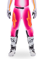 Alpinestars Limited Edition Supertech AFD MIG Pants, pantaloni da motocross, rosa fluo e bianco con accenti arancioni, caratterizzati da grandi loghi a stella sulle cosce, pannelli perforati e zone di grip nere sulle ginocchia, indossati con stivali da motocross bianchi e neri