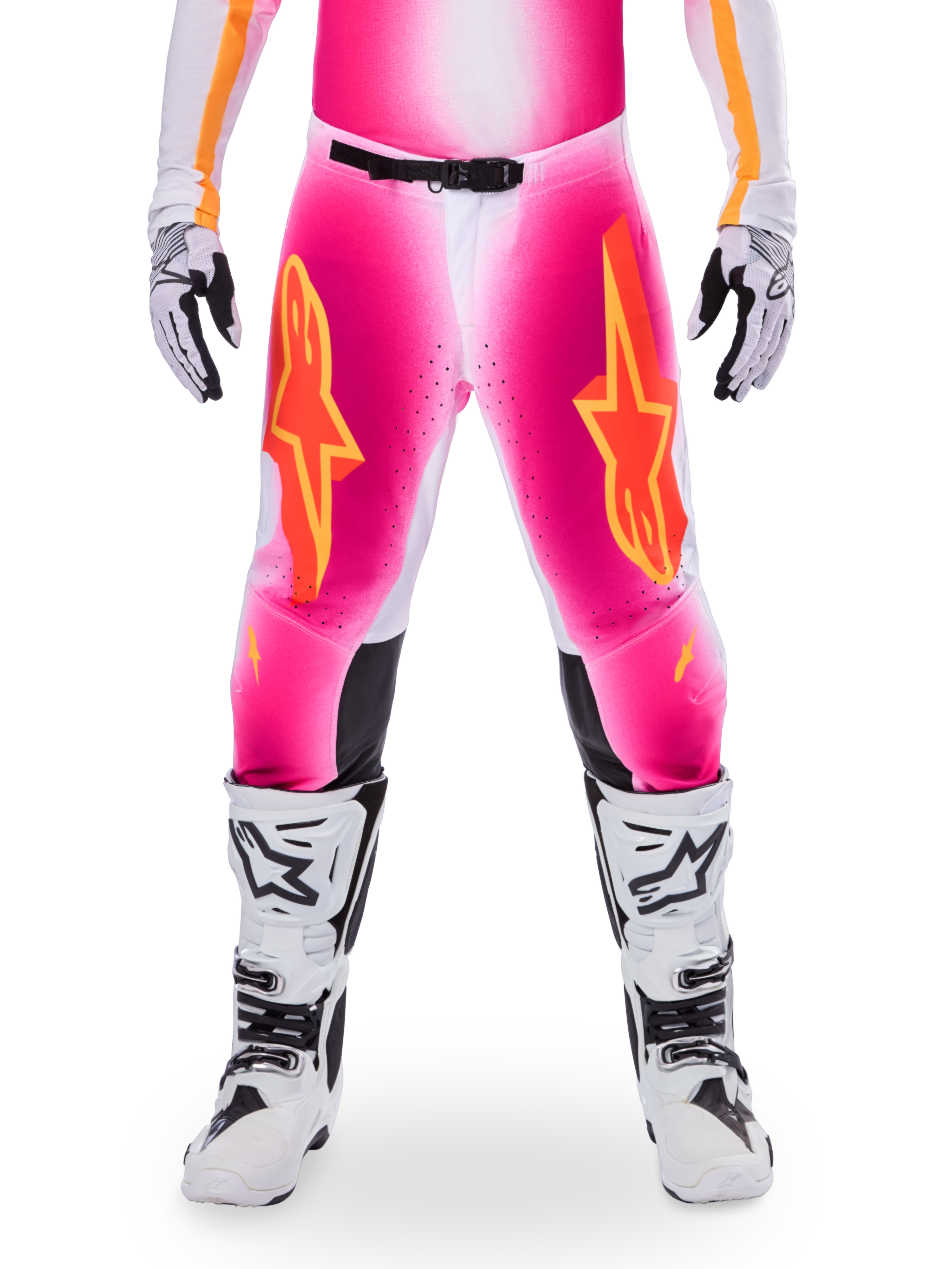 Alpinestars Limited Edition Supertech AFD MIG Pants, pantaloni da motocross, rosa fluo e bianco con accenti arancioni, caratterizzati da grandi loghi a stella sulle cosce, pannelli perforati e zone di grip nere sulle ginocchia, indossati con stivali da motocross bianchi e neri