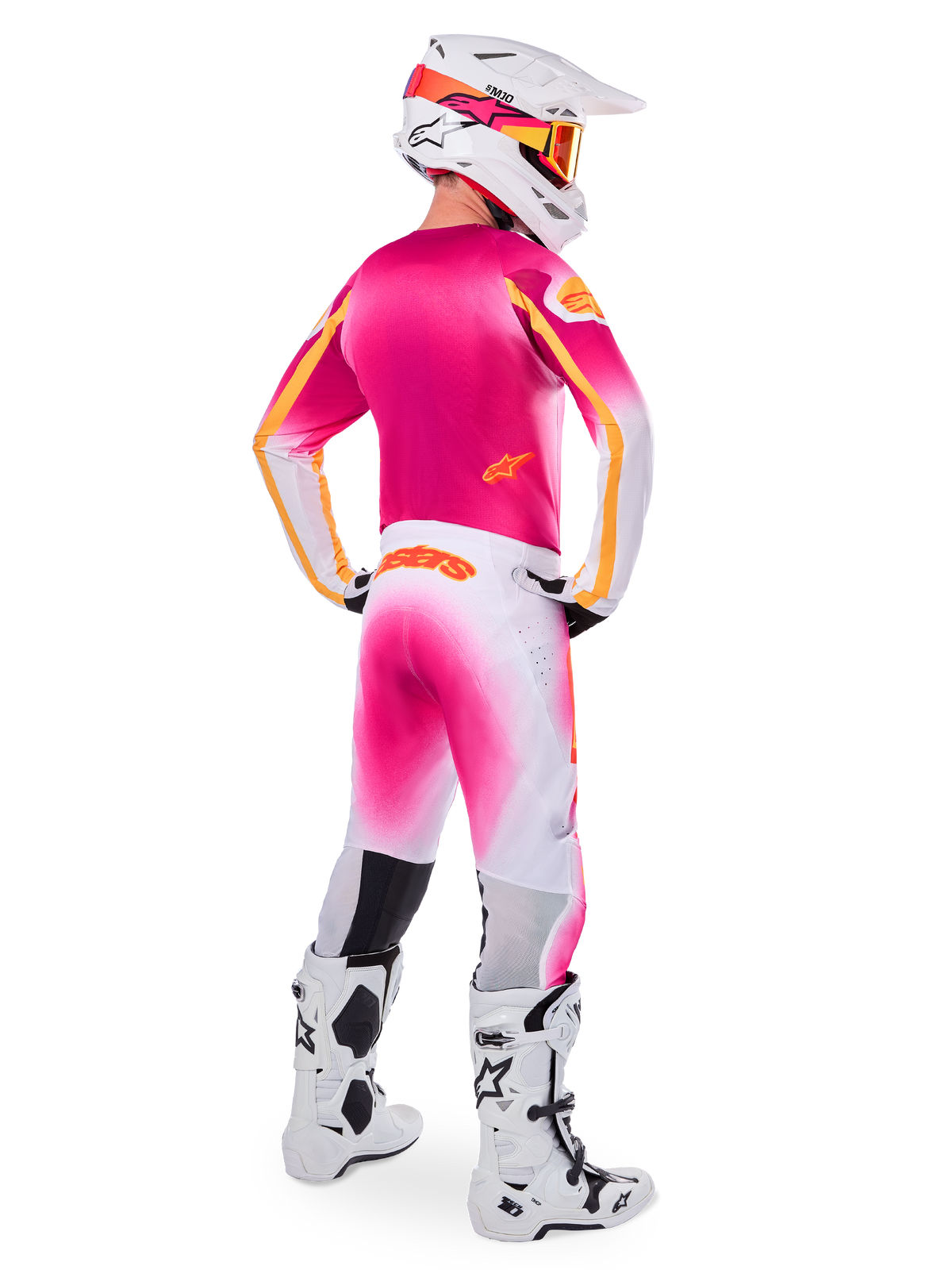 Pilota di motocross visto di spalle che indossa il set Limited Edition Supertech AFD MIG, maglia rosa con accenti arancioni, pantaloni bianchi con sfumatura rosa e marchio Alpinestars arancione, casco bianco con grafiche rosa e maschera arancione, stivali bianchi e neri, kit da corsa professionale per fuoristrada
