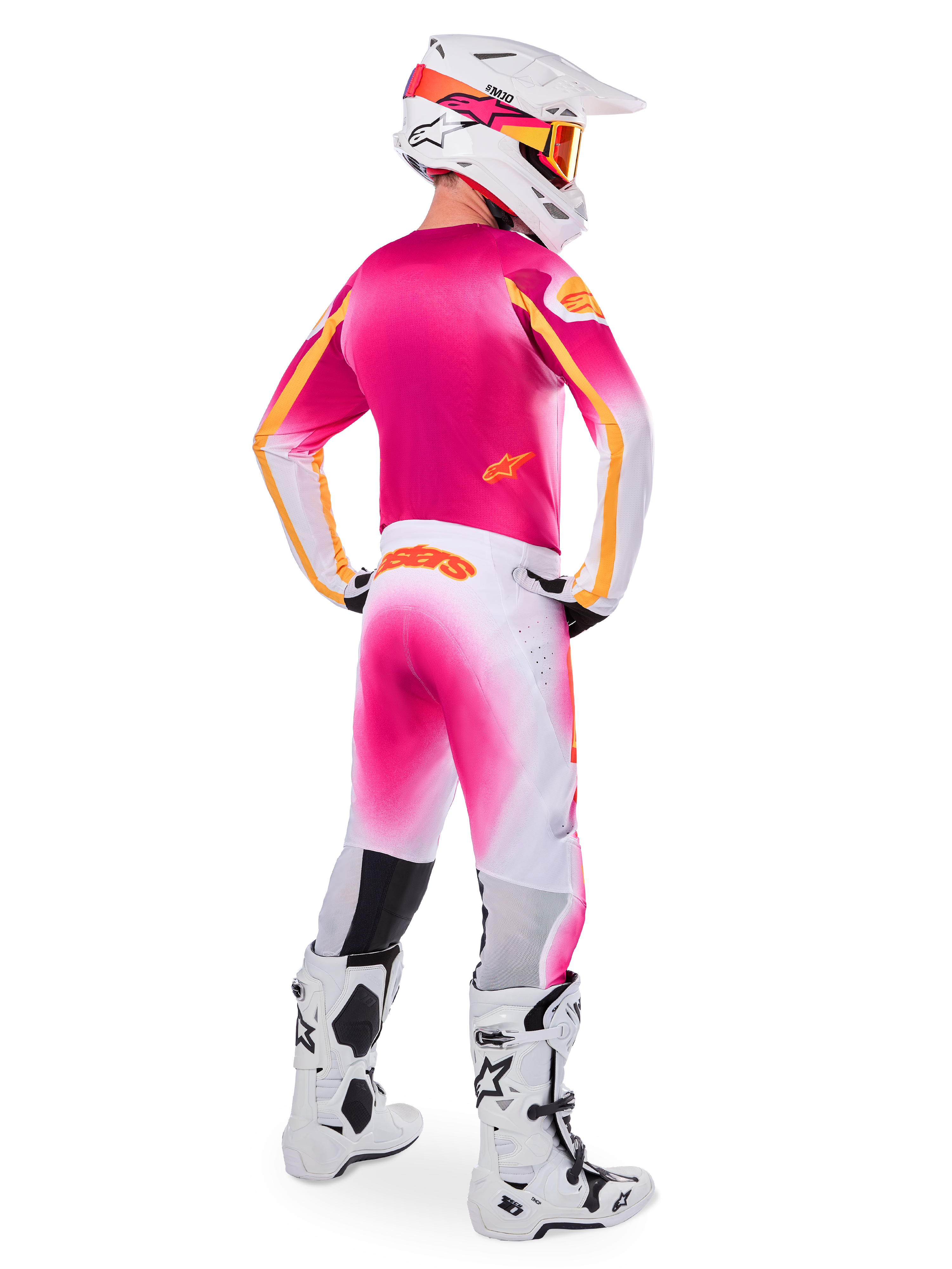 Pilota di motocross visto di spalle che indossa il set Limited Edition Supertech AFD MIG, maglia rosa con accenti arancioni, pantaloni bianchi con sfumatura rosa e marchio Alpinestars arancione, casco bianco con grafiche rosa e maschera arancione, stivali bianchi e neri, kit da corsa professionale per fuoristrada