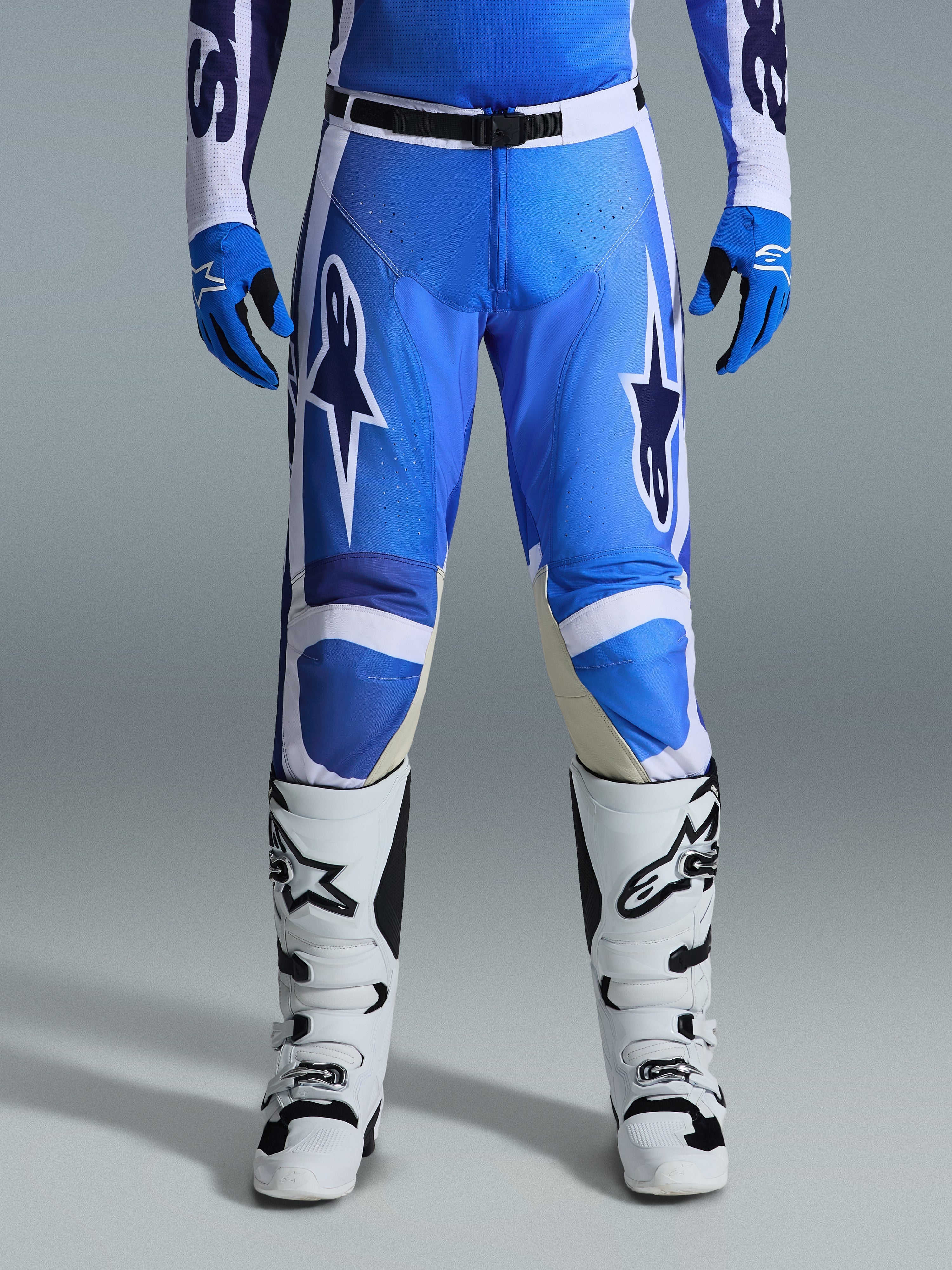 Alpinestars 2026 Racer Air Portl Pants, pantaloni da motocross, blu UCLA e bianco, indossati con guanti blu coordinati e stivali bianchi, caratterizzati da chiusura in vita nera, grandi loghi a stella bianchi sulle cosce e tessuto traforato per un maggiore flusso d'aria durante le corse off-road.