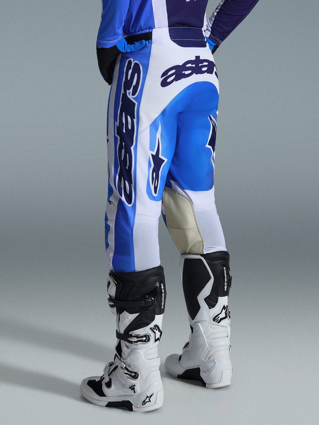 Alpinestars 2026 Racer Air Portl Pants, pantaloni da motocross, Ucla Blue White, vista posteriore, design audace blu e bianco con grande branding sulla seduta e sul lato, interno ginocchia in pelle di capra rinforzata, indossati con stivali da motocross bianchi e neri per prestazioni off-road.