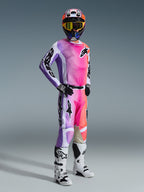 Pilota di motocross con maglia Alpinestars Racer Air Portl 2026 e pantaloni coordinati, sfumatura multicolore rosa, viola e arancione con accenti bianchi, casco colorato e maschera gialla coordinati, stivali bianchi e neri, completo da gara per prestazioni off-road