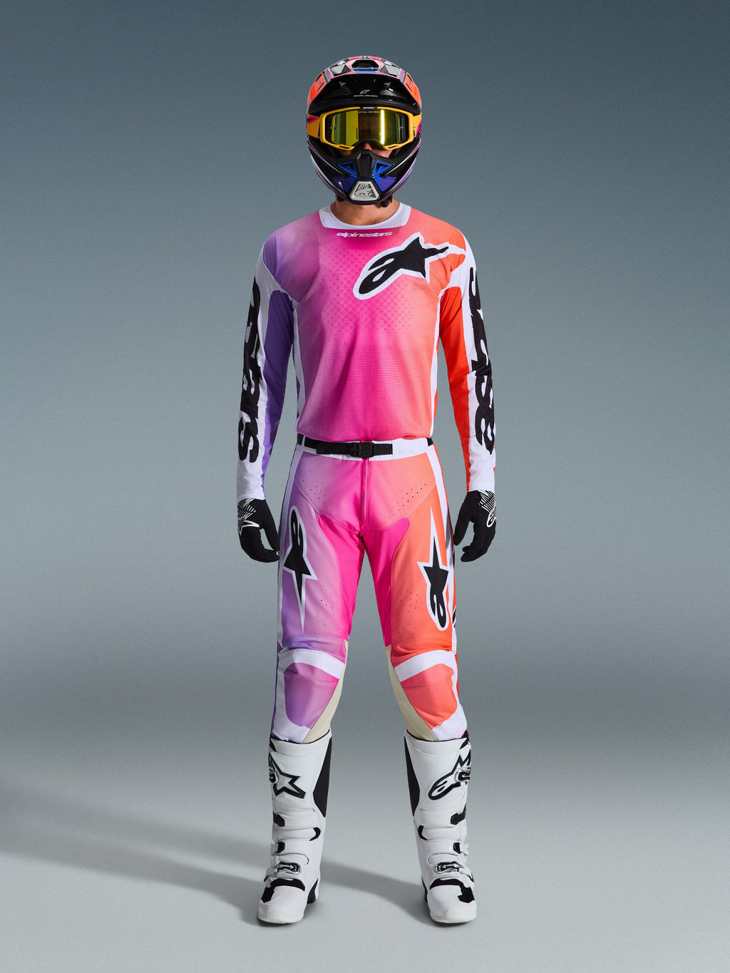Alpinestars Set completo Racer Air Portl 2026, abbigliamento da motocross, rosa, viola e arancione, completo di casco coordinato, occhiali con lenti gialle, guanti neri e stivali bianchi, con logo a stella nero sul petto e sulle gambe.