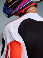 Alpinestars 2026 Racer Air Portl Jersey, maglia da motocross, multicolore con pannelli bianchi, neri e rossi, primo piano della struttura in mesh traforato su spalla e schiena per la ventilazione, indossata con un casco da motocross colorato