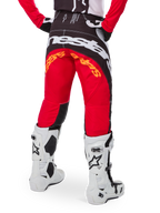 Alpinestars Techstar Deep Pants Edizione Limitata, pantaloni da motocross, nero, bianco e rosso acceso, vista posteriore con grande logo Alpinestars bianco sulla seduta e dettagli arancioni, indossati con stivali tecnici bianchi per competizioni fuoristrada professionistiche.