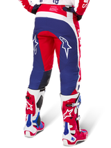Pantaloni Alpinestars Limited Edition Techstar Fortitude, pantaloni da motocross, rosso, bianco e blu, vista posteriore indossati con stivali coordinati rossi e bianchi, con loghi a stella bianchi sulle cosce, design multi-pannello resistente per gare off-road professionali