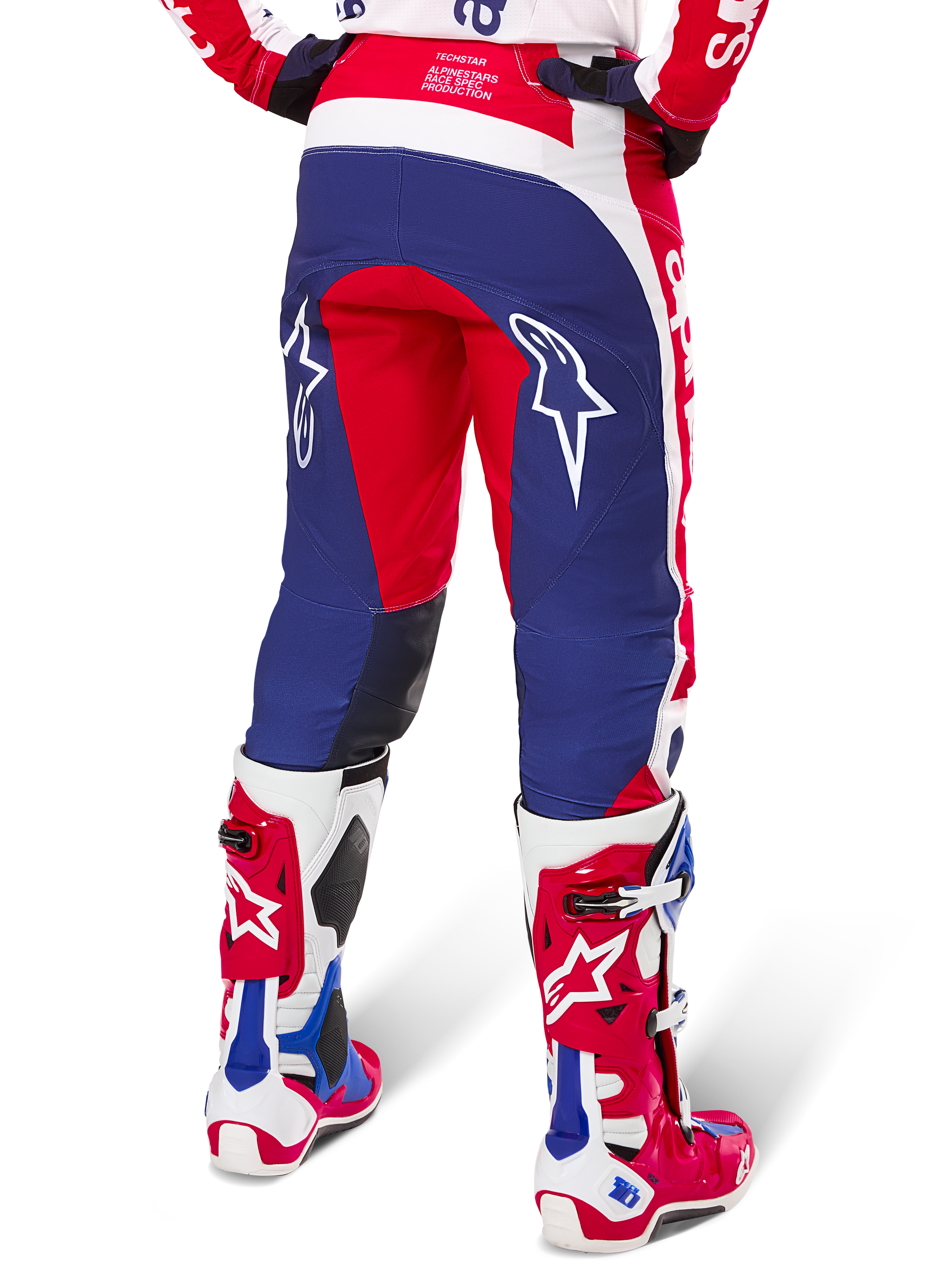 Pantaloni Alpinestars Limited Edition Techstar Fortitude, pantaloni da motocross, rosso, bianco e blu, vista posteriore indossati con stivali coordinati rossi e bianchi, con loghi a stella bianchi sulle cosce, design multi-pannello resistente per gare off-road professionali