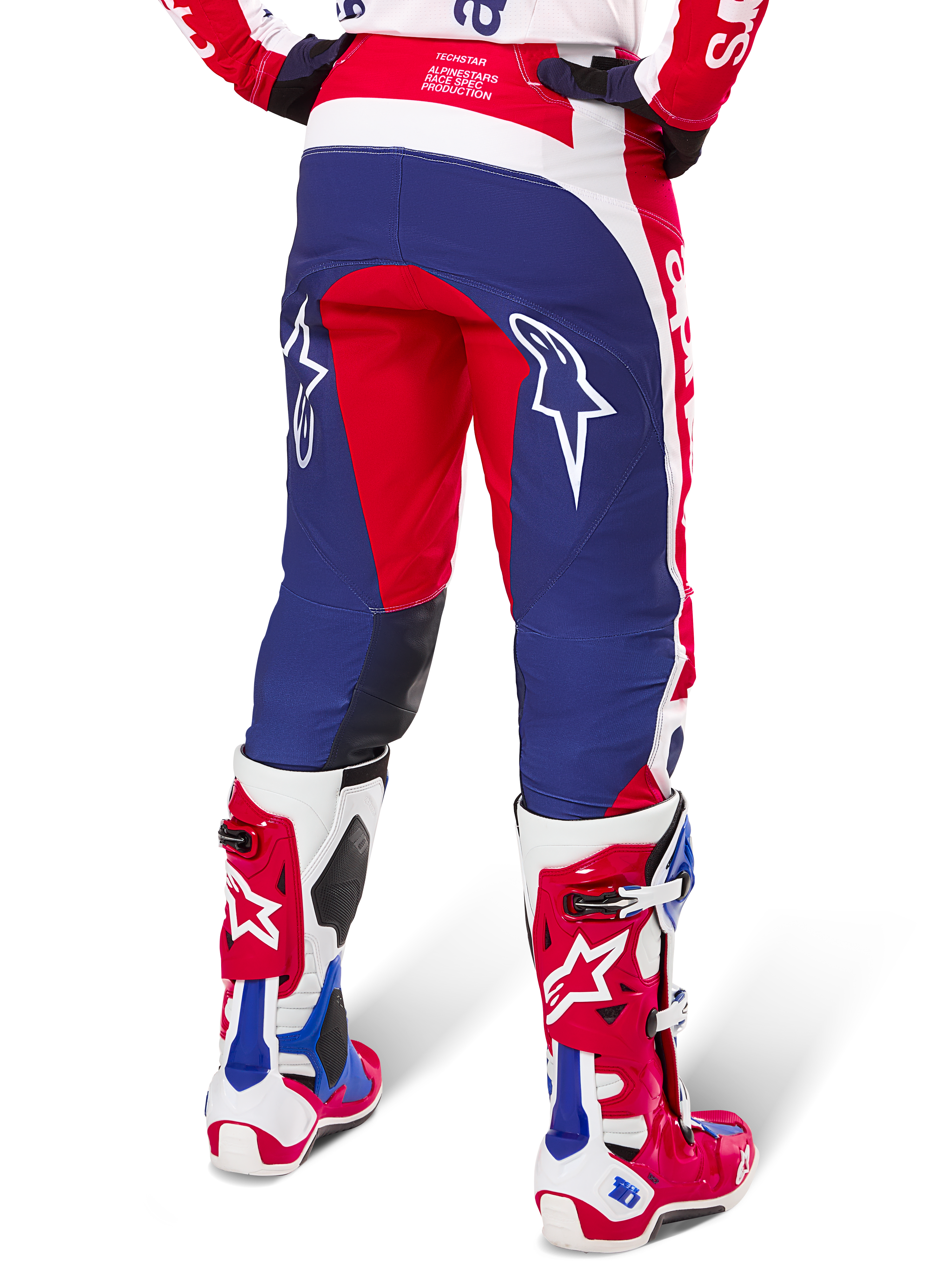 Pantaloni Alpinestars Limited Edition Techstar Fortitude, pantaloni da motocross, rosso, bianco e blu, vista posteriore indossati con stivali coordinati rossi e bianchi, con loghi a stella bianchi sulle cosce, design multi-pannello resistente per gare off-road professionali