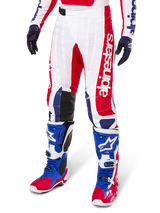 Alpinestars Limited Edition Techstar Fortitude Pants, pantaloni da motocross, rosso acceso, bianco e blu, indossati con stivali e guanti da fuoristrada coordinati, caratterizzati da marchio verticale sulla gamba, pannelli traforati traspiranti e sezioni rinforzate nere sulle ginocchia, design con vestibilità atletica da gara.