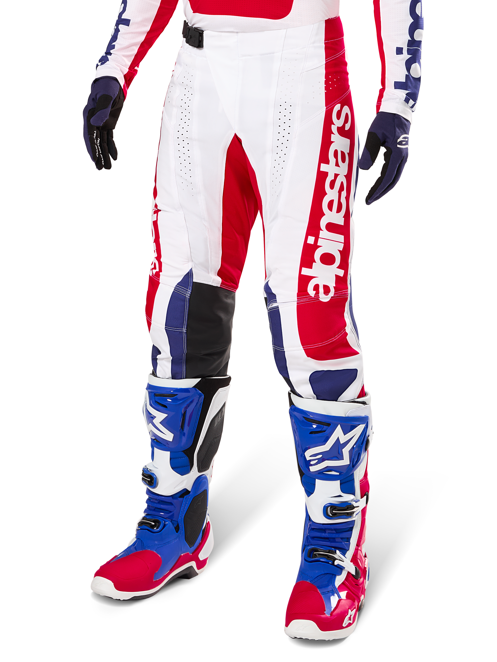 Alpinestars Limited Edition Techstar Fortitude Pants, pantaloni da motocross, rosso acceso, bianco e blu, indossati con stivali e guanti da fuoristrada coordinati, caratterizzati da marchio verticale sulla gamba, pannelli traforati traspiranti e sezioni rinforzate nere sulle ginocchia, design con vestibilità atletica da gara.