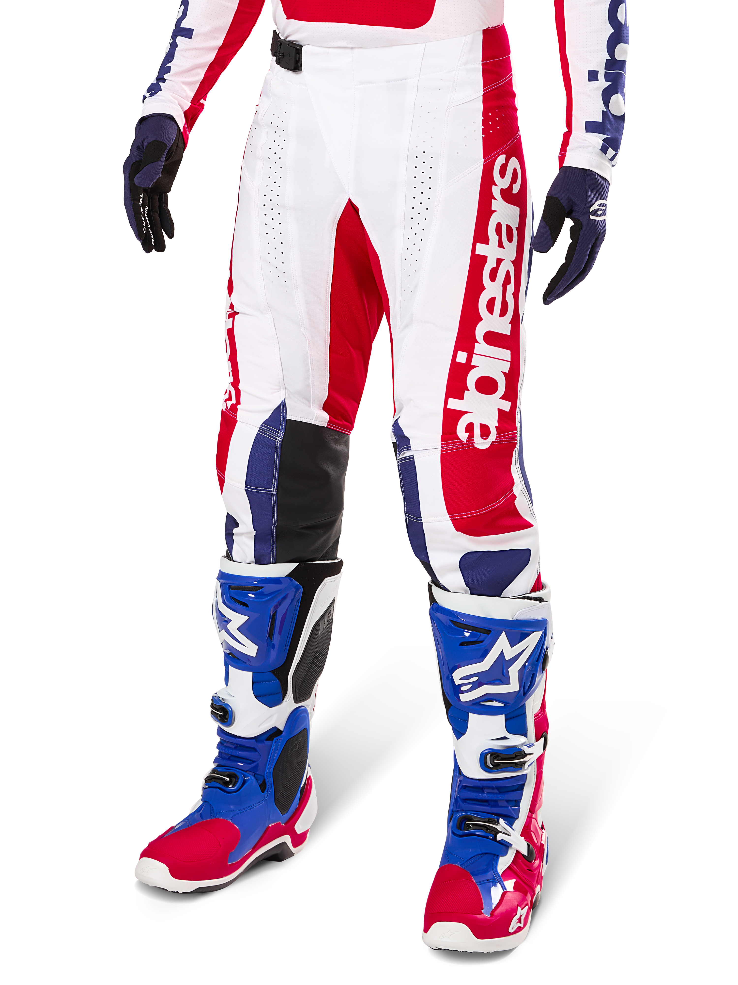 Alpinestars Limited Edition Techstar Fortitude Pants, pantaloni da motocross, rosso acceso, bianco e blu, indossati con stivali e guanti da fuoristrada coordinati, caratterizzati da marchio verticale sulla gamba, pannelli traforati traspiranti e sezioni rinforzate nere sulle ginocchia, design con vestibilità atletica da gara.