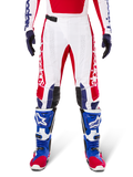 Alpinestars Limited Edition Techstar Fortitude Pants, pantaloni da motocross, rosso acceso, bianco e blu, indossati con equipaggiamento coordinato comprensivo di stivali protettivi e guanti blu, base bianca con grafiche rosse, pannelli sulle ginocchia in pelle nera e perforazioni al laser, abbigliamento professionale da gara fuoristrada