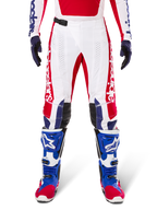 Alpinestars Limited Edition Techstar Fortitude Pants, pantaloni da motocross, rosso acceso, bianco e blu, indossati con equipaggiamento coordinato comprensivo di stivali protettivi e guanti blu, base bianca con grafiche rosse, pannelli sulle ginocchia in pelle nera e perforazioni al laser, abbigliamento professionale da gara fuoristrada