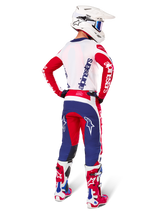 Alpinestars Techstar Fortitude Edizione Limitata, pantaloni da motocross, rosso acceso, bianco e blu, mostrati di spalle su un pilota con maglia, stivali e casco coordinati, che evidenziano la vestibilità atletica e il posizionamento audace del logo.