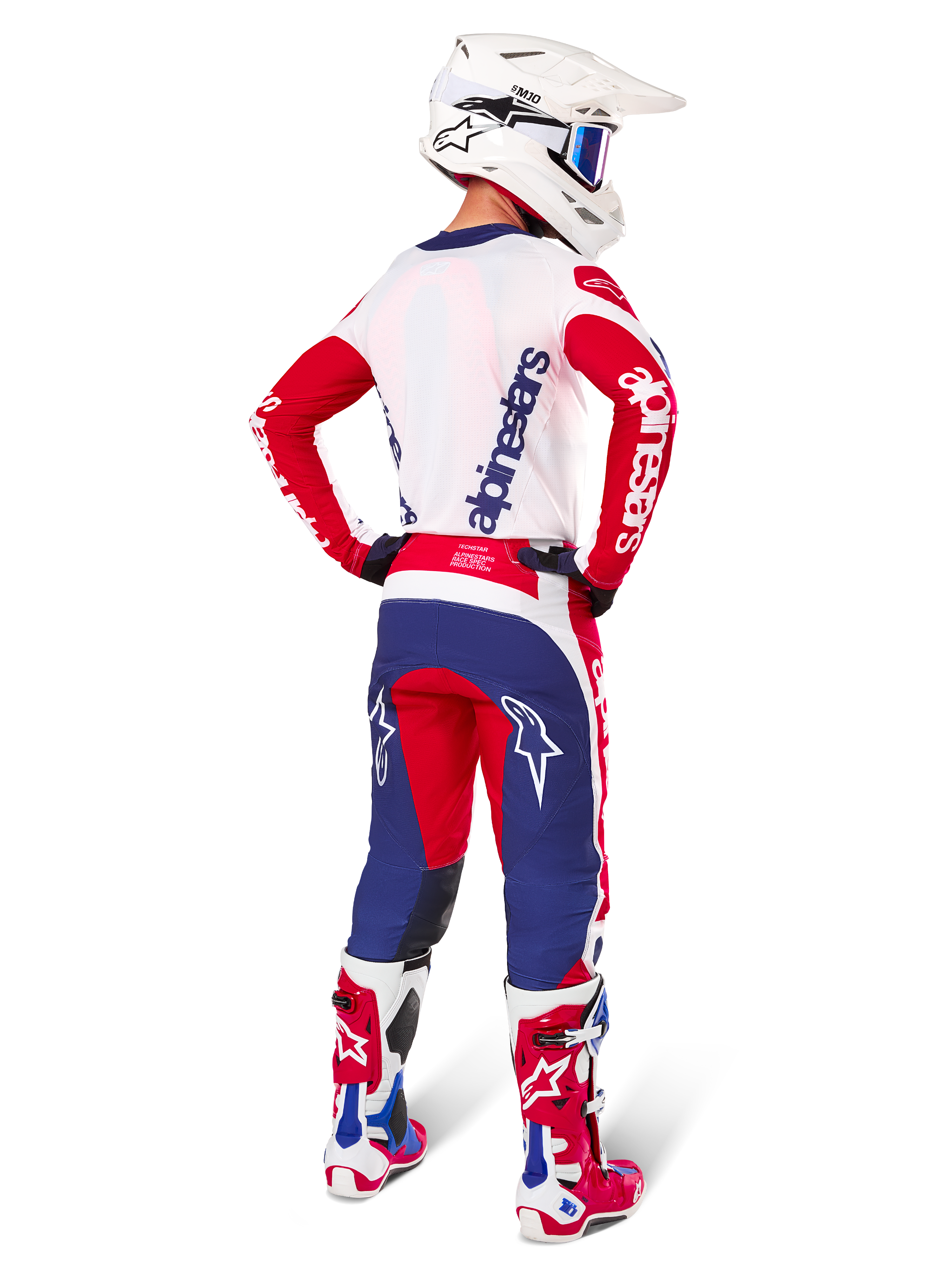Alpinestars Techstar Fortitude Edizione Limitata, pantaloni da motocross, rosso acceso, bianco e blu, mostrati di spalle su un pilota con maglia, stivali e casco coordinati, che evidenziano la vestibilità atletica e il posizionamento audace del logo.