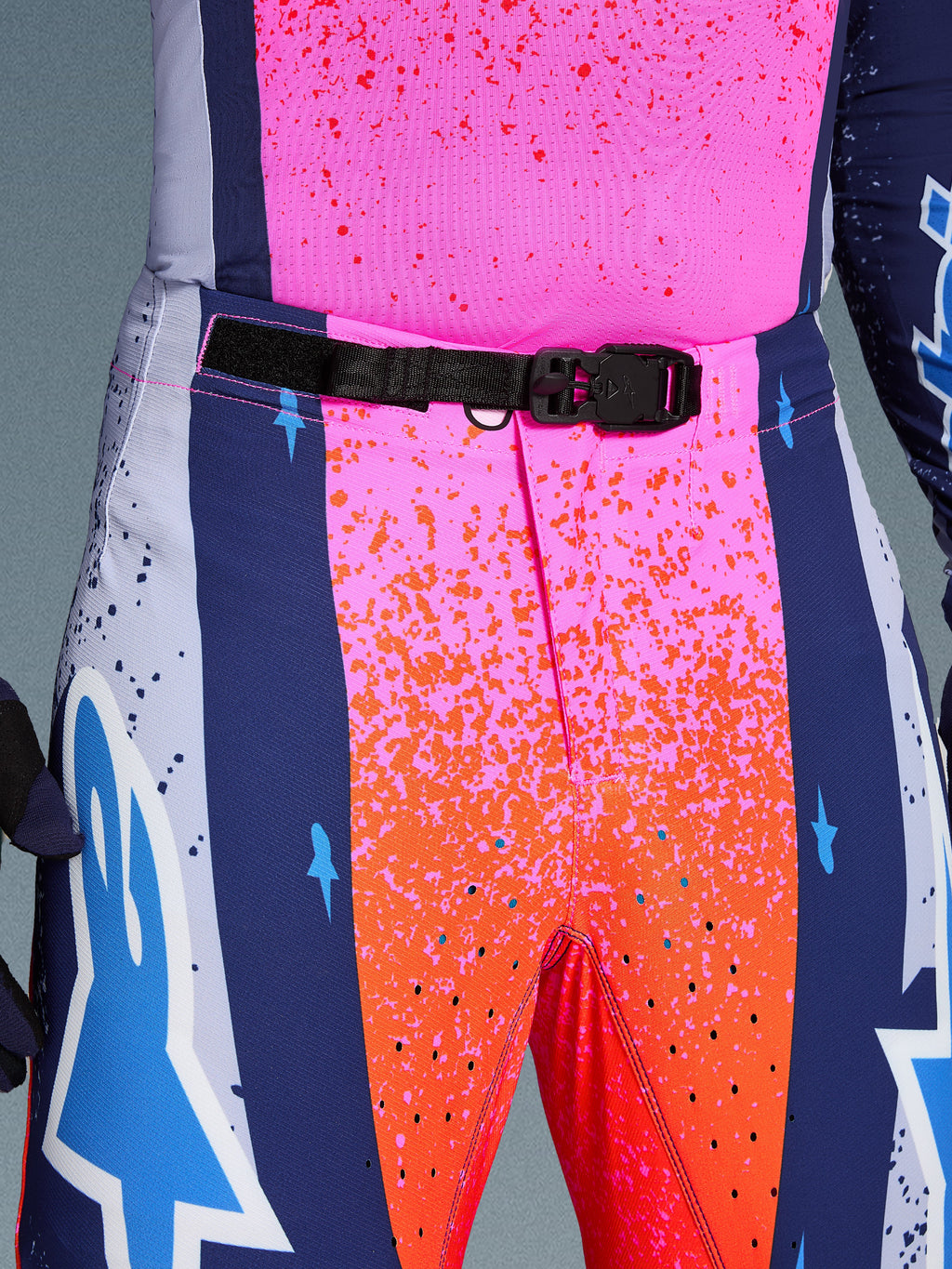 Alpinestars Limited Edition Supertech Records Pants, pantaloni da motocross, multicolore rosa e arancione con pannelli laterali blu navy, primo piano della vita con fibbia magnetica SX1 nera, tessuto rip-stop con grafiche splatter e perforazioni laser.