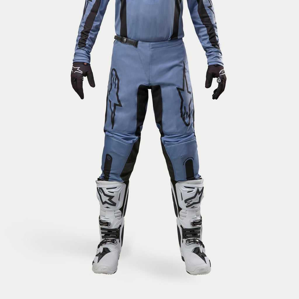 Alpinestars Pantaloni Fluid Lurv 2024, pantaloni da motocross, azzurro e nero, indossati con stivali da corsa bianchi e neri e guanti coordinati, con vistosi loghi a stella neri sulle cosce, design ergonomico per prestazioni off-road