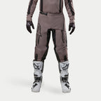 Pantaloni Alpinestars Fluid Lurv 2024, pantaloni da motocross, Mud Black, indossati con maglia coordinata, guanti neri e stivali bianchi, caratterizzati da grandi loghi neri sulle cosce, vestibilità ergonomica e materiale resistente per corse fuoristrada
