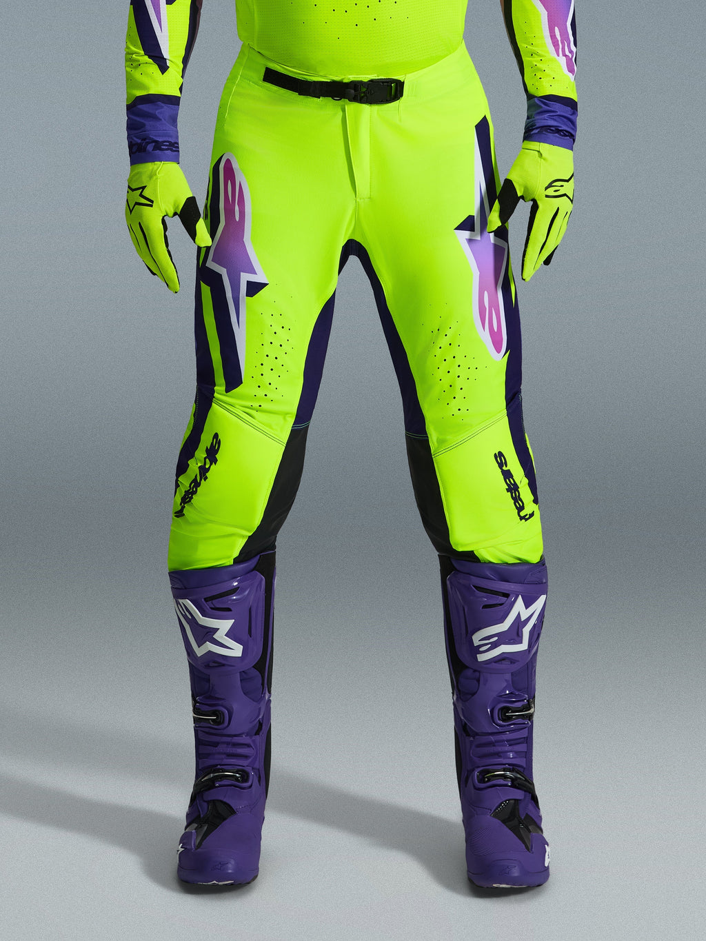 Alpinestars Pantaloni Supertech Vista 2026, pantaloni da motocross, giallo fluorescente, viola e nero, indossati con guanti coordinati e stivali viola, con grandi loghi sfumati sulle cosce, zone perforate per la ventilazione e design atletico professionale per gare off-road