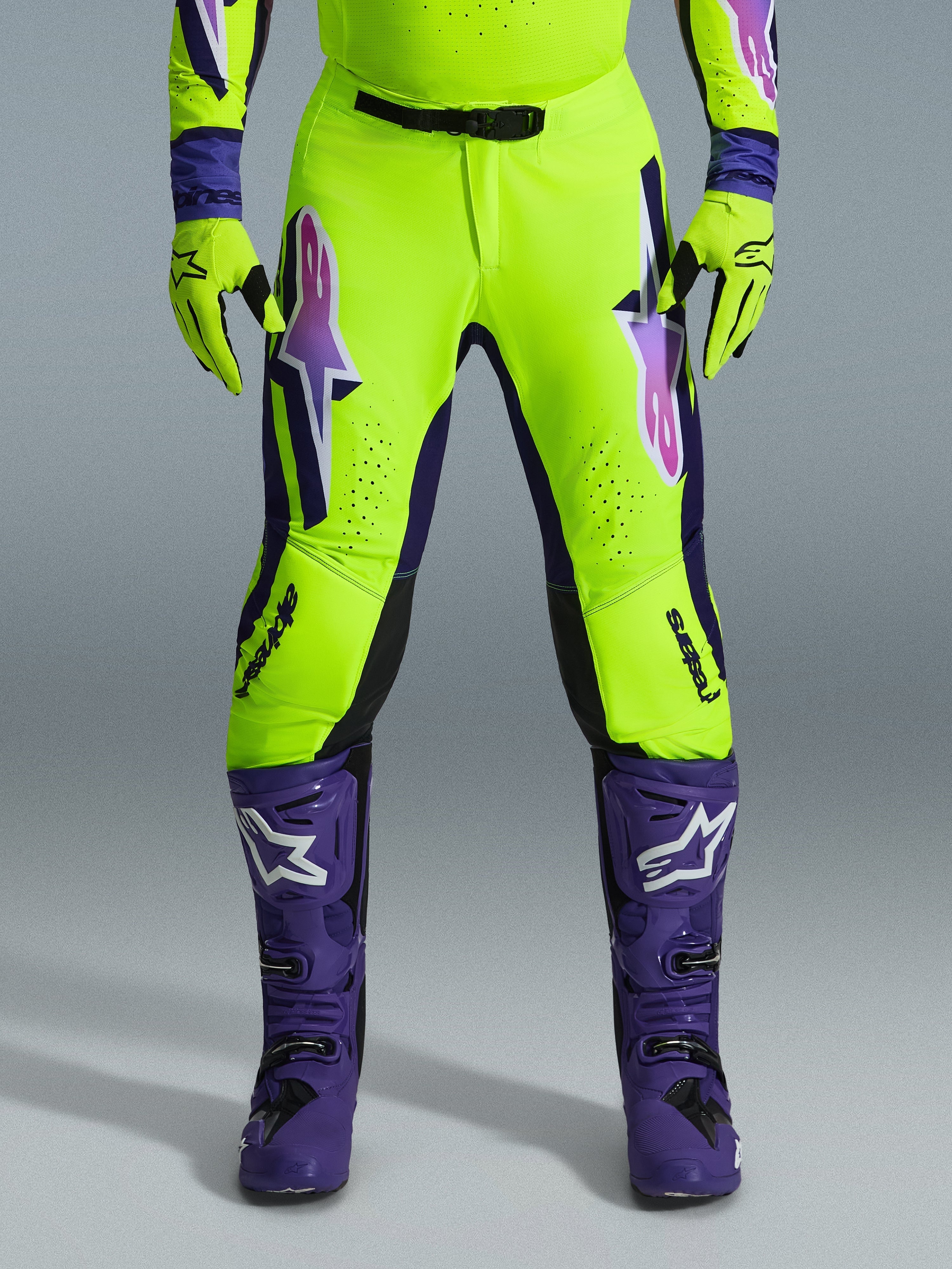 Alpinestars Pantaloni Supertech Vista 2026, pantaloni da motocross, giallo fluorescente, viola e nero, indossati con guanti coordinati e stivali viola, con grandi loghi sfumati sulle cosce, zone perforate per la ventilazione e design atletico professionale per gare off-road