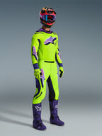 Pilota di motocross che indossa la Maglia Supertech Vista 2026, giallo acceso con dettagli viola e neri, pantaloni da motocross gialli coordinati, stivali viola e guanti gialli, casco multicolore con maschera blu, abbigliamento tecnico ad alte prestazioni per competizioni fuoristrada