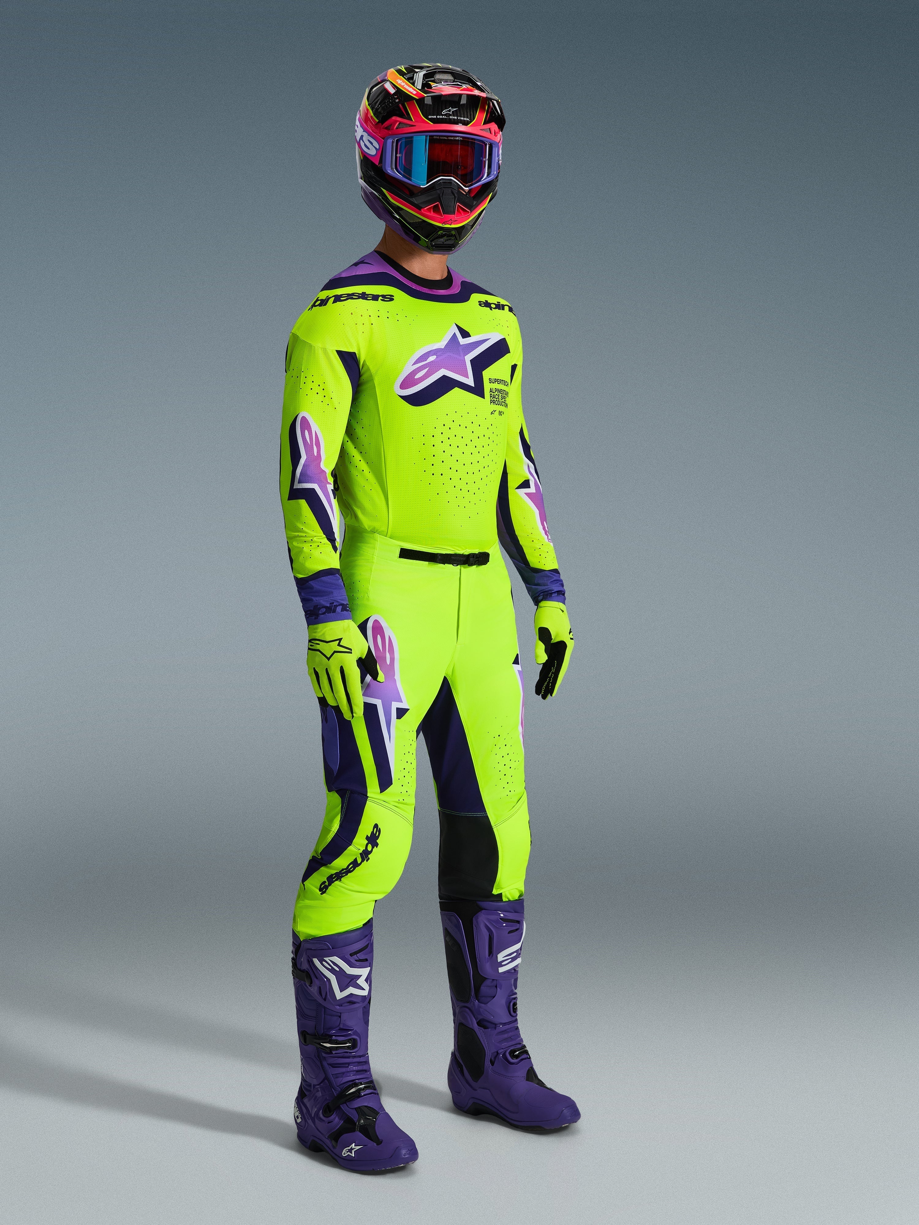 Pilota di motocross che indossa la Maglia Supertech Vista 2026, giallo acceso con dettagli viola e neri, pantaloni da motocross gialli coordinati, stivali viola e guanti gialli, casco multicolore con maschera blu, abbigliamento tecnico ad alte prestazioni per competizioni fuoristrada