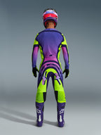 Alpinestars 2026 Supertech Vista Pants, pantaloni da motocross, giallo, viola e nero, vista posteriore di un pilota di motocross con set completo di abbigliamento da gara, maglia con sfumatura viola e stivali viola, design atletico per competizioni off-road professionali